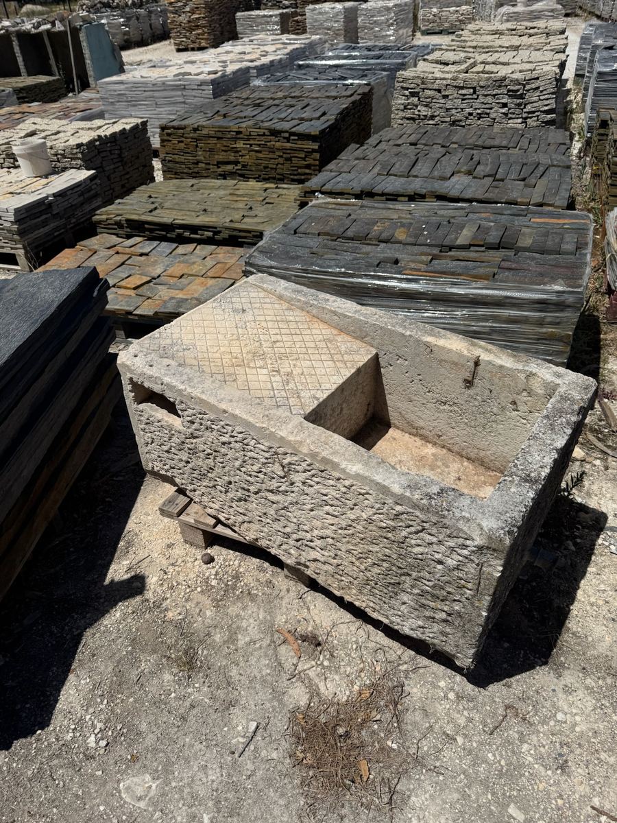 Antique carved stone trough beside reclaimed stone tiles
