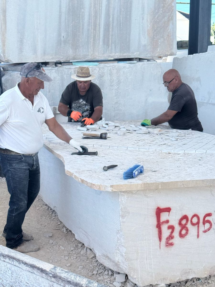 Masons hand-finishing a marble block at the quarry